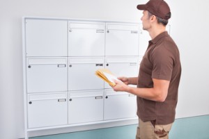 Portrait Of Mature Postman Putting Letters In Mailbox